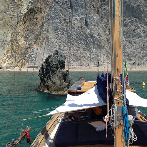 Il caicco alla fonda in una baia di Ponza, con lo scoglio e la falesia alle spalle