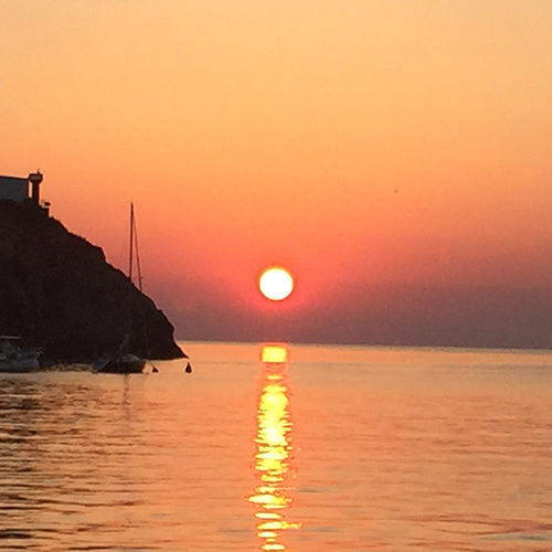 Tramonto rosso sul mare di Ponza, con il promontorio e una barca a vela