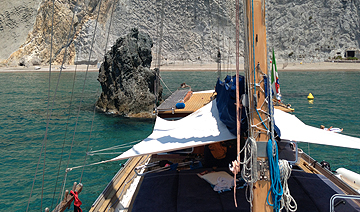 Prua del caicco davanti a uno scoglio e alle falesie bianche di Ponza