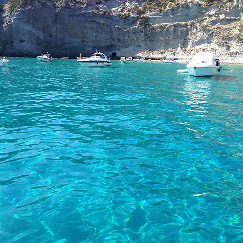 Barche alla fonda nel mare turchese sotto le falesie bianche di Palmarola