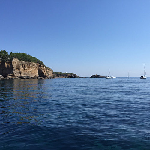 La costa rocciosa di Ventotene con barche a vela in lontananza
